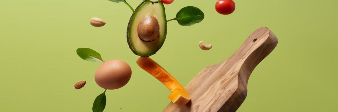 A creative arrangement of paleo diet ingredients floating above a wooden board on a green background.